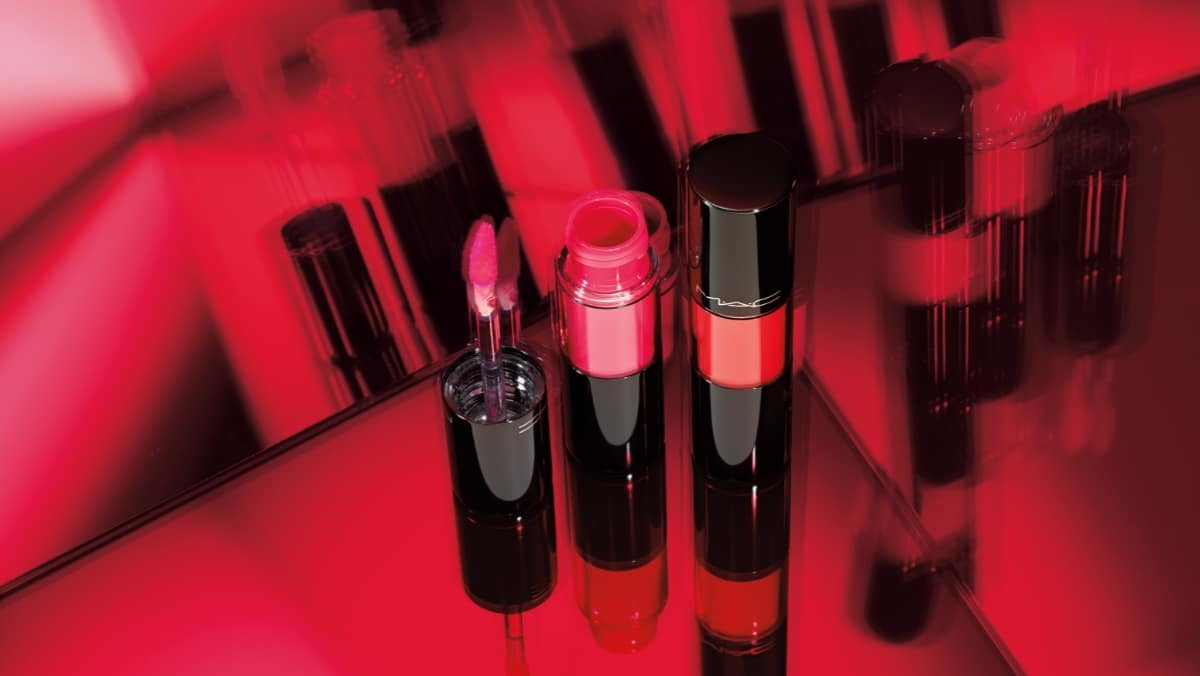 Beauty 11 - 50_50 An open lip gloss and lipstick in shades of red stand upright against a reflective red and black background, resembling a stunning 3D printing model.