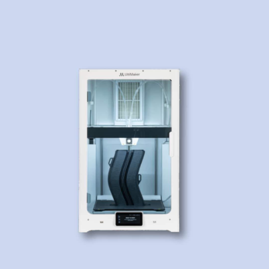 A 3D printer in operation printing two large black objects inside a transparent enclosure, against a plain light blue background.