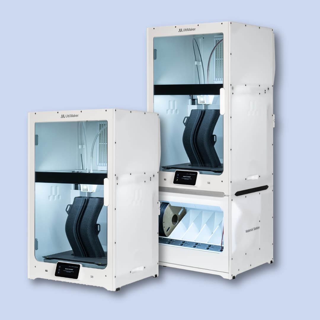 Two Ultimaker S5 3D printers are shown on a light blue background; one printer includes a lower storage unit with drawers for filament spools.